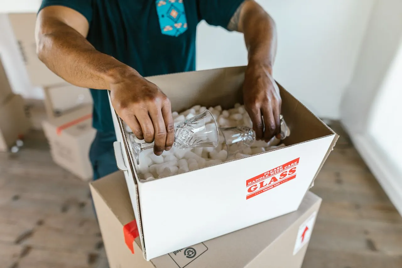 A mover packing glassware into a carton marked Fragile, Handle With Care