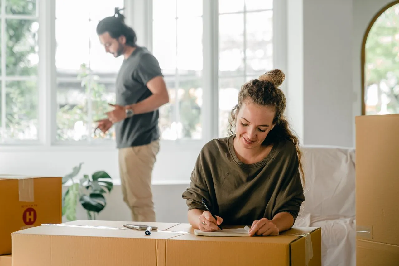 A couple reading through moving paperwork spread across a packed cardboard box